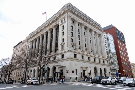 Street view of an iconic historic building in Washington D.C. with cars and pedestrians on a sunny day.