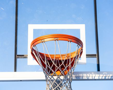 Close-up of an orange basketball hoop and net against a clear blue sky.